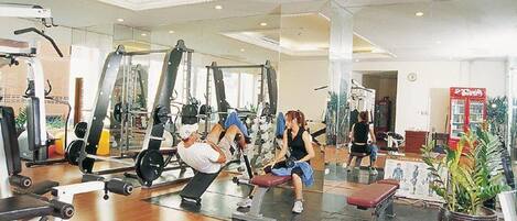 A gym with various exercise equipment, a mirrored wall, and a Coca-Cola vending machine.