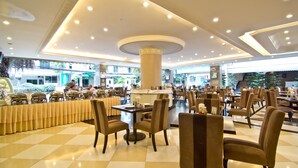 A spacious indoor dining area with multiple tables and chairs, a central decorative column, and a checkered floor pattern. - LK Royal Suite Pattaya (Pattaya)