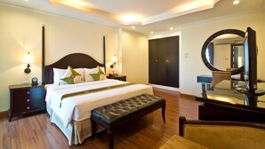 A hotel room with a large bed, a bench, a nightstand, a dresser, a mirror, and a door. - LK Royal Suite Pattaya (Pattaya)