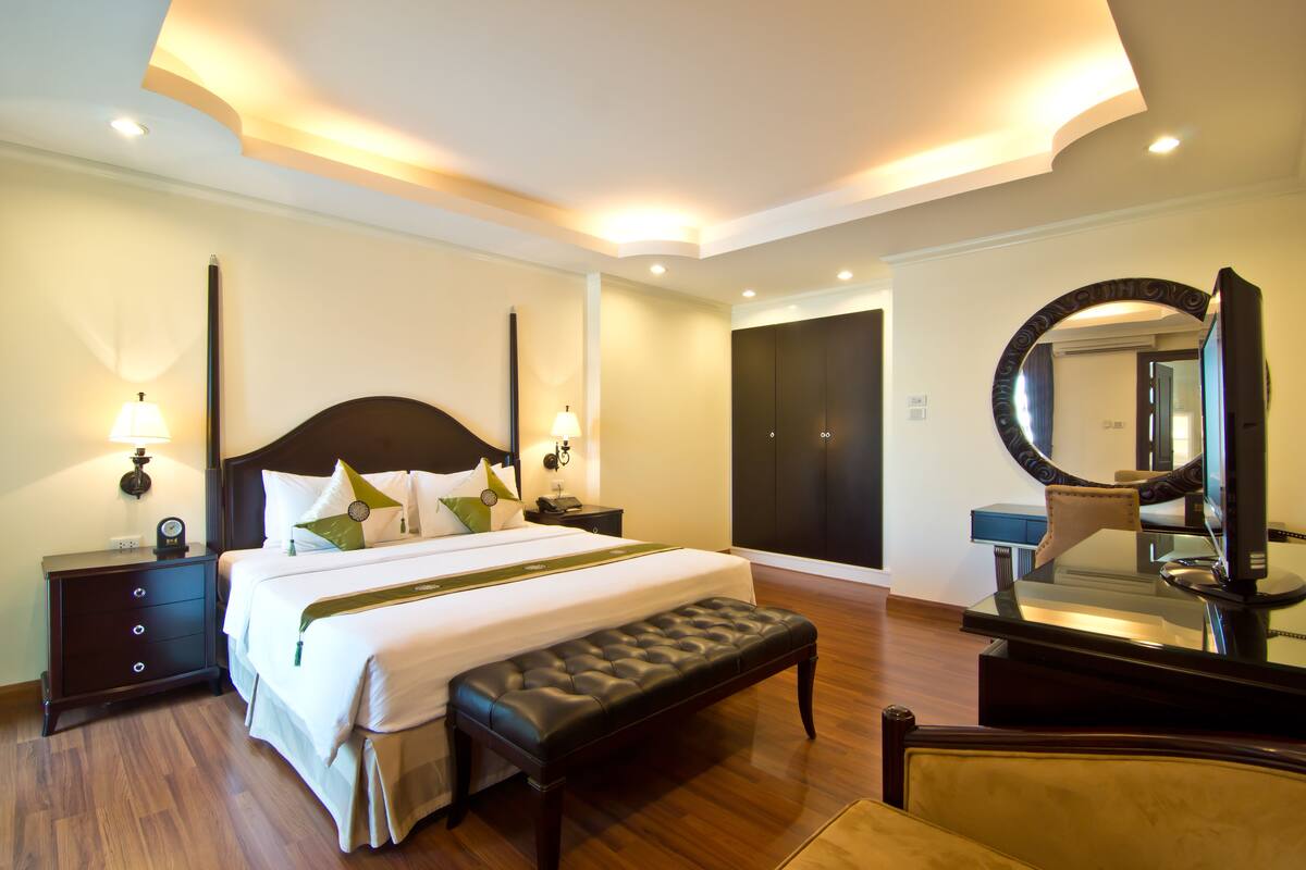 A hotel room with a large bed, a bench, a nightstand, a dresser, a mirror, and a door.