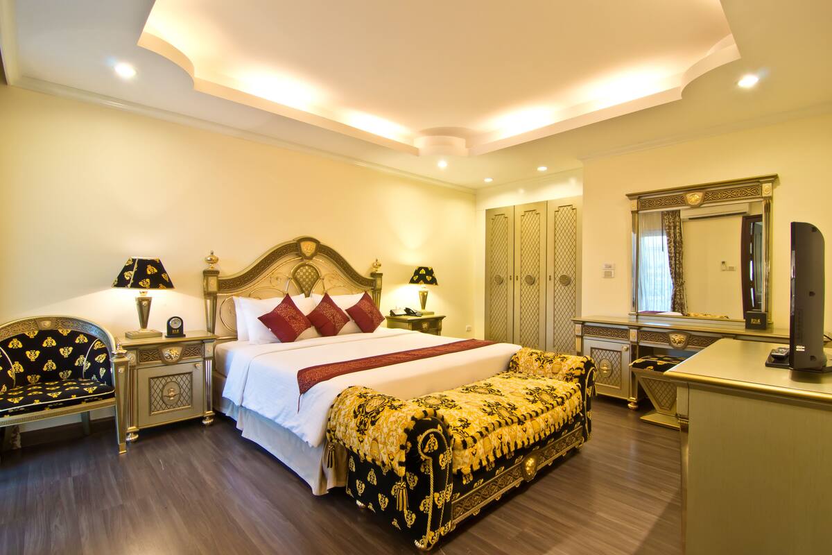 A well-lit bedroom with a large bed, bedside tables, a desk, and a wardrobe.