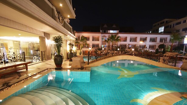 A swimming pool with a curved edge, surrounded by a decorative railing and potted plants. - LK Royal Suite Pattaya (Pattaya)