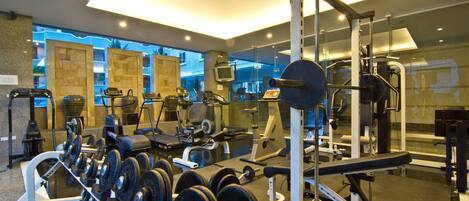 Ein Fitnessstudio mit verschiedenen Trainingsgeräten, darunter Laufbänder, Kraftgeräte und Kurzhanteln.