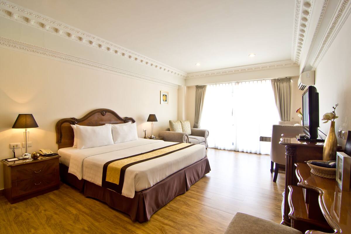 A hotel room with a large bed, a desk, a chair, and a television.