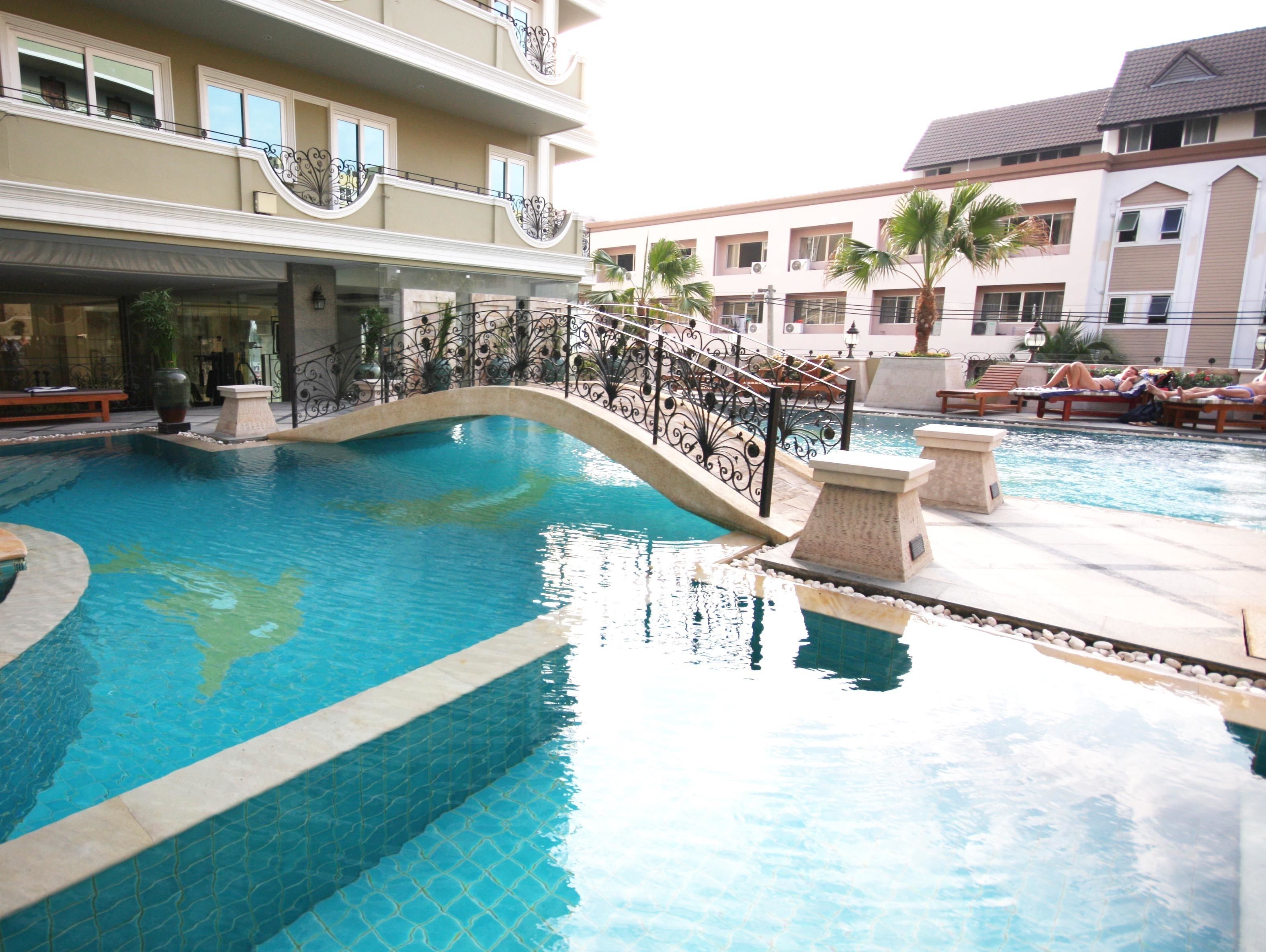 A swimming pool with a curved design, surrounded by a stone deck and metal railings.