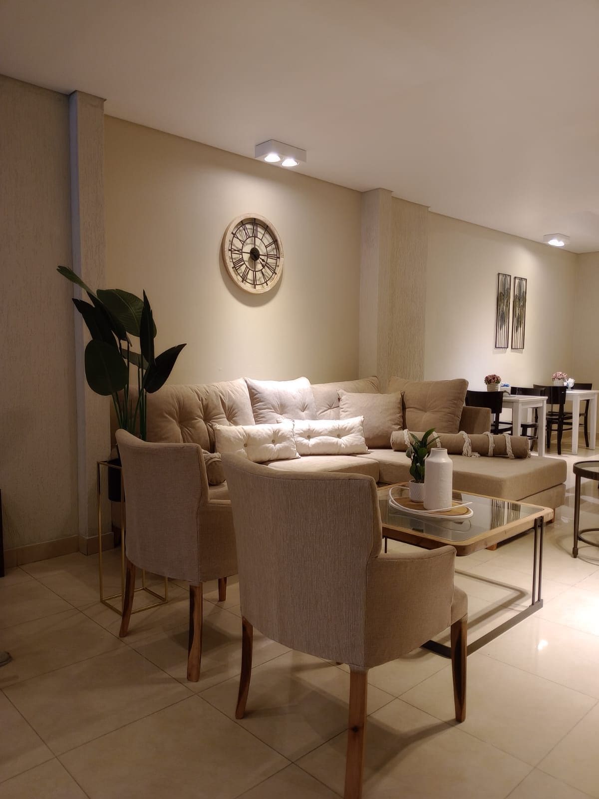 Una sala de estar moderna con un sofá color beige, dos sillones, una mesa de centro y un comedor al fondo.