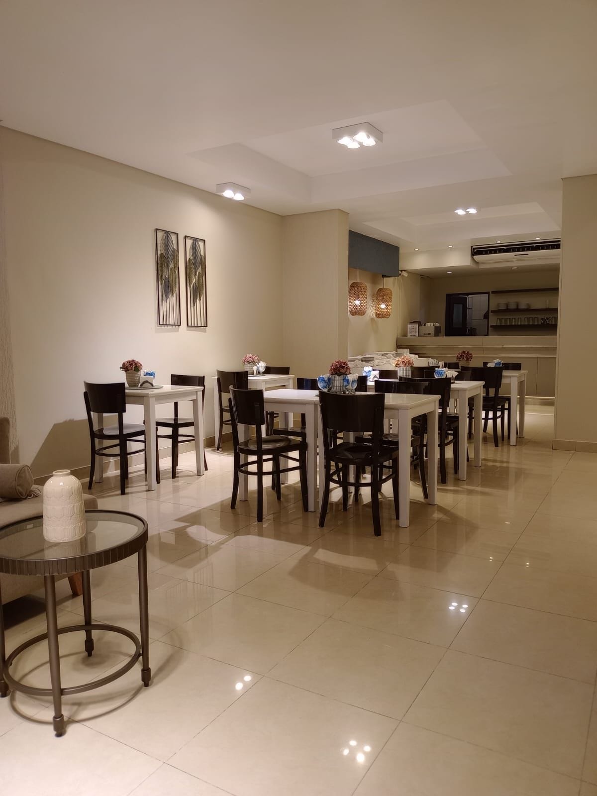 Un comedor con varias mesas y sillas, una zona de cocina al fondo e iluminación empotrada en el techo.