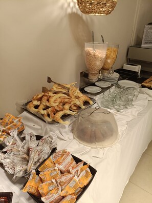 A buffet table with various food items, including pastries, sandwiches, and a covered dish, likely for a hotel breakfast service. - Viasui Hotel (Buenos Aires)