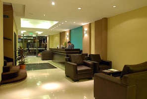 Un vestíbul d'hotel amb taulell de recepció, zona de seients i una escala.