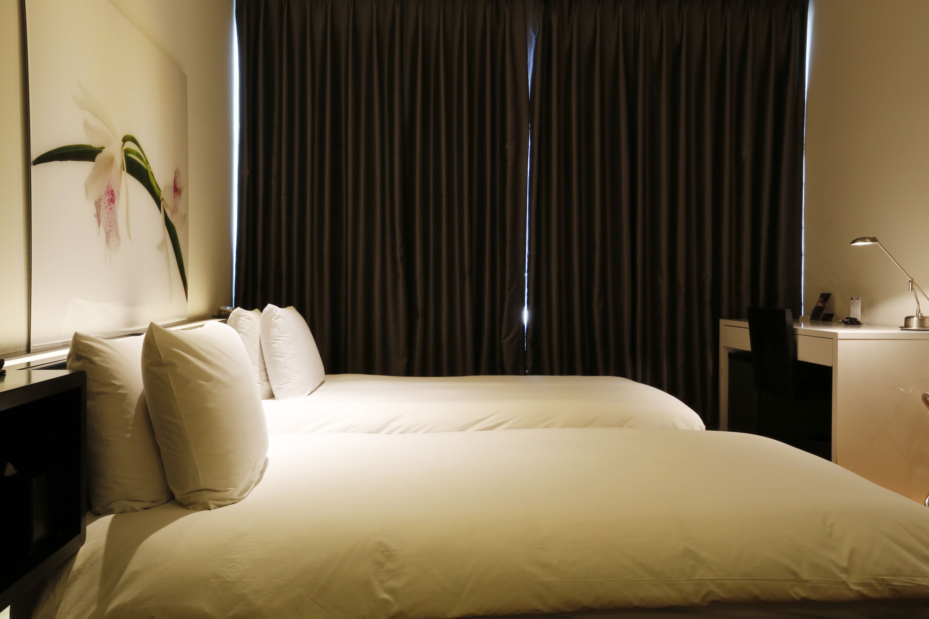 Una habitación de hotel con una cama grande, un escritorio, una lámpara y un cuadro de una orquídea en la pared.