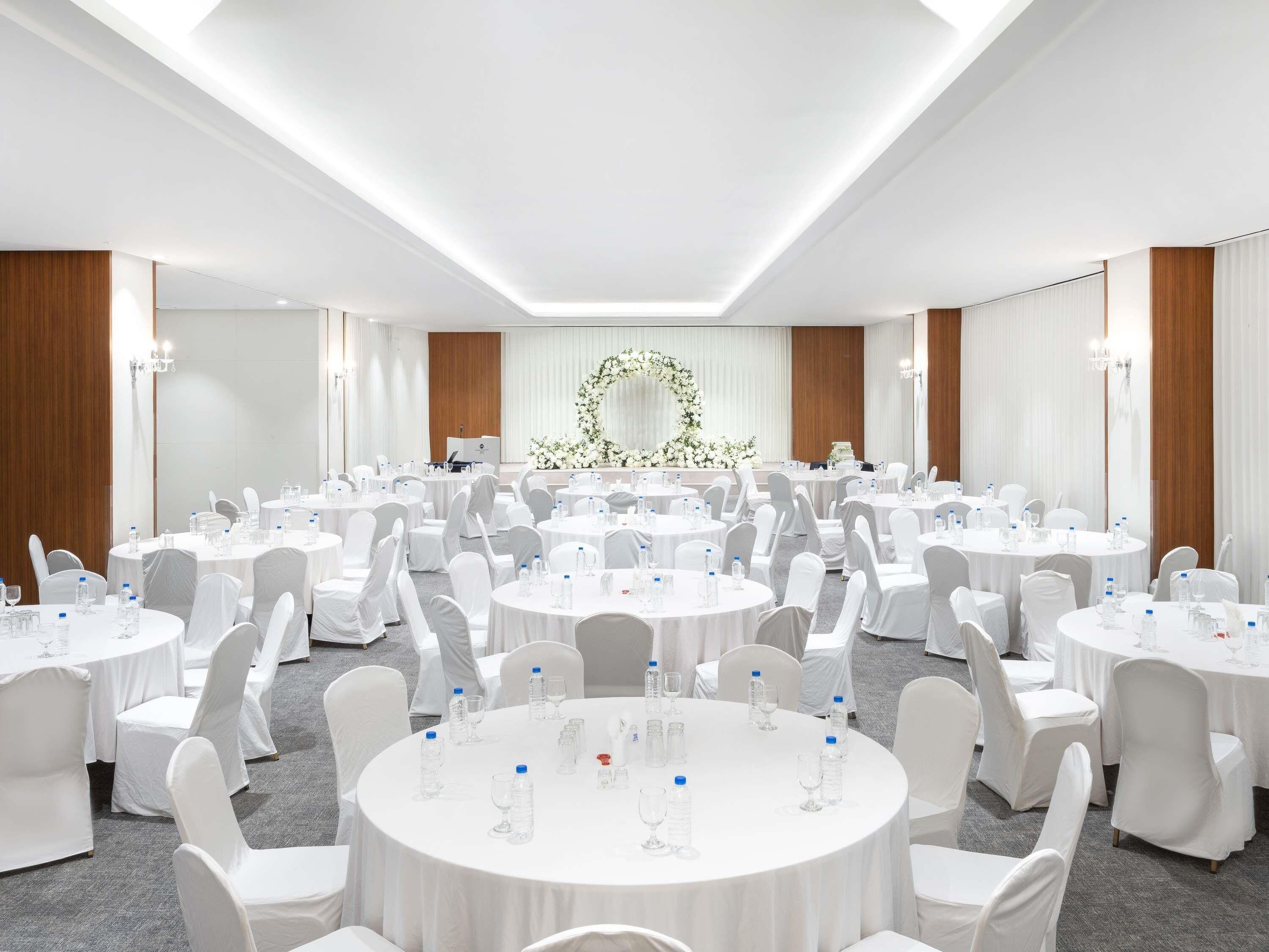A conference room with round tables, white chairs, and a floral arrangement at the front.