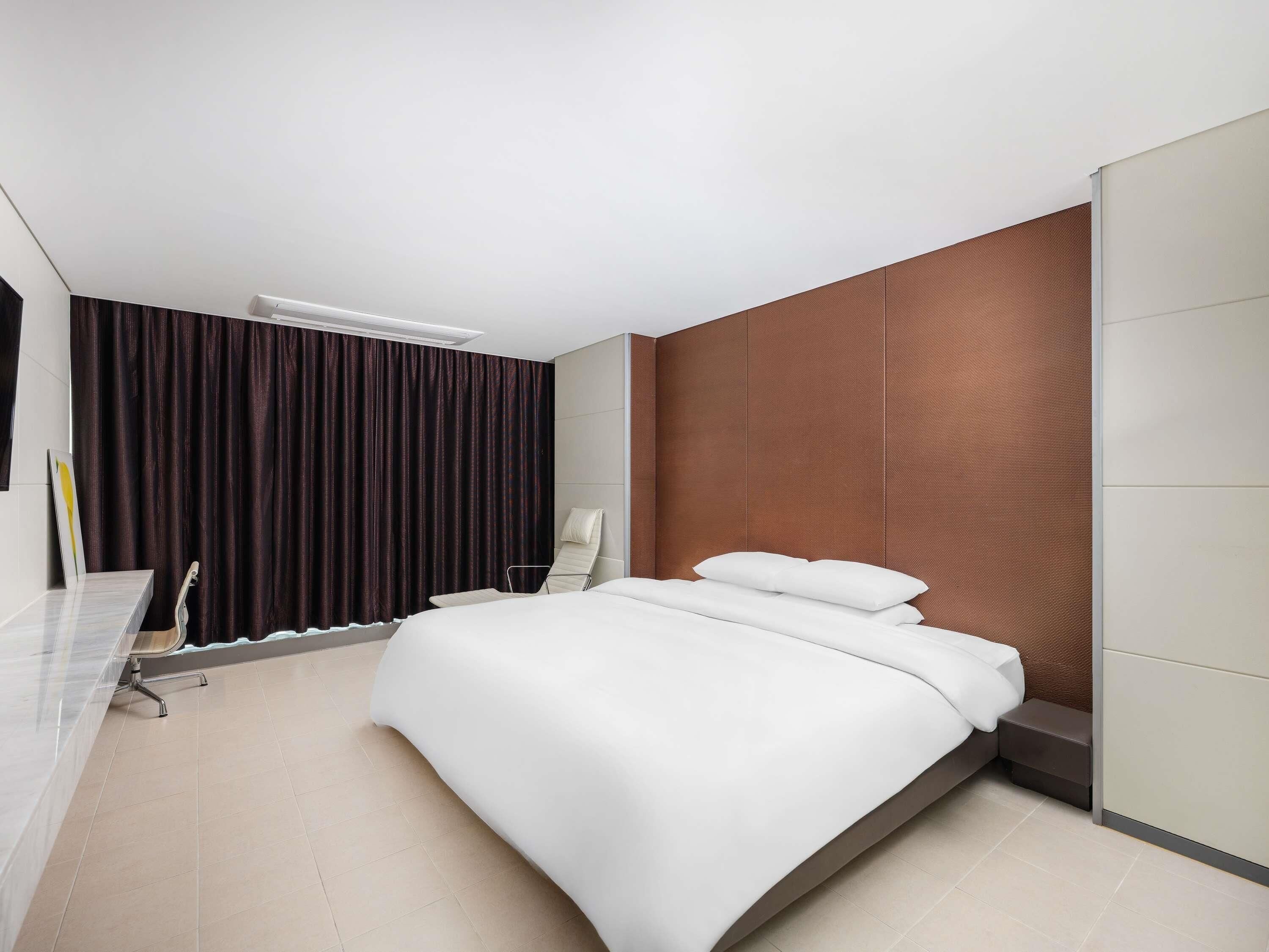 A modern hotel room with a bed, a desk, and a chair.