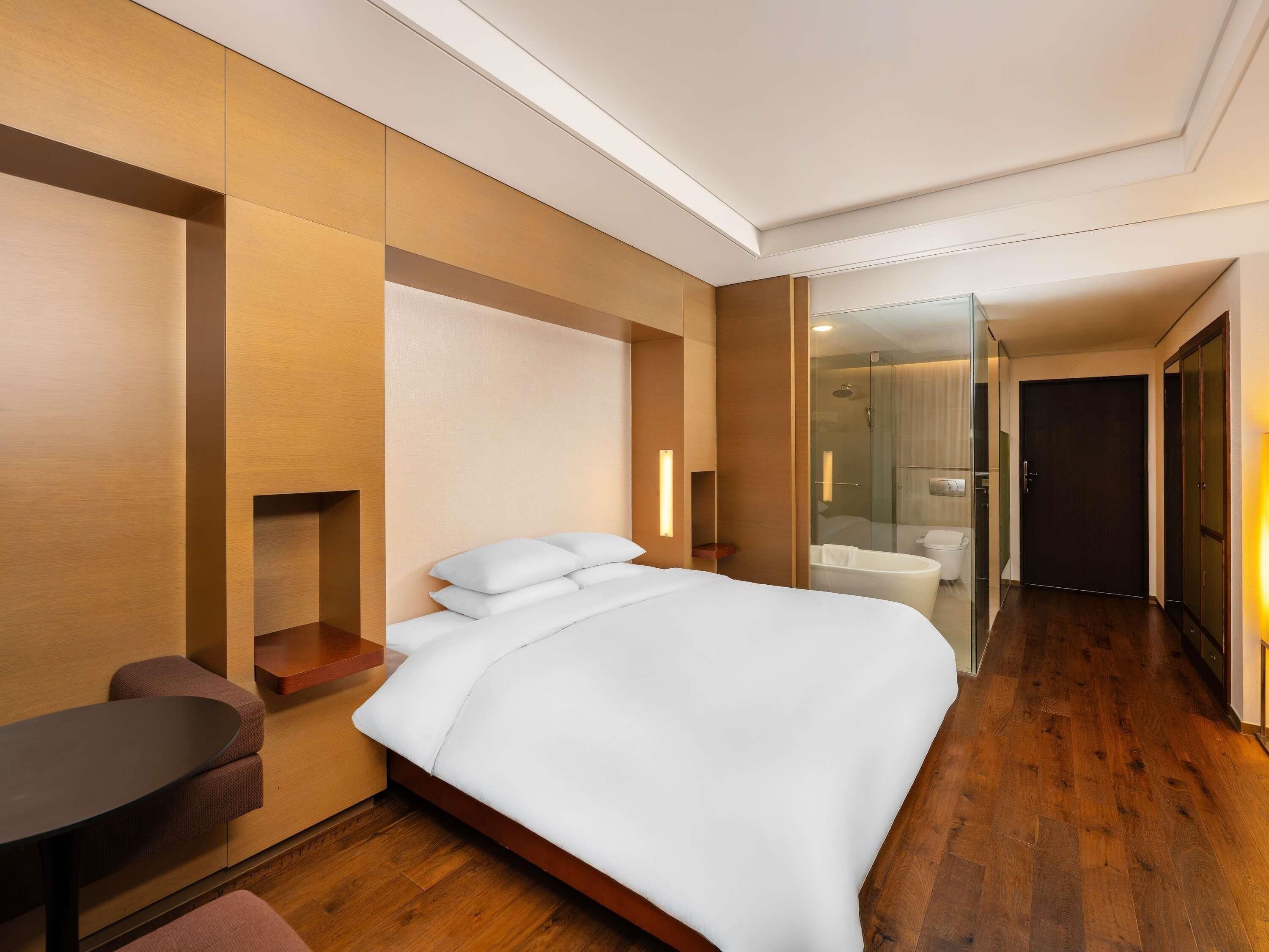 Una habitación de hotel con cama, escritorio, silla y baño con ducha.