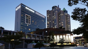 A hotel with a modern glass facade, a prominent sign, and a nearby high-rise building. - Grand Mercure Ambassador Changwon (Changwon)