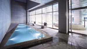 A modern indoor pool with clear glass walls, stone flooring, and a minimalist design. - Grand Mercure Ambassador Changwon (Changwon)