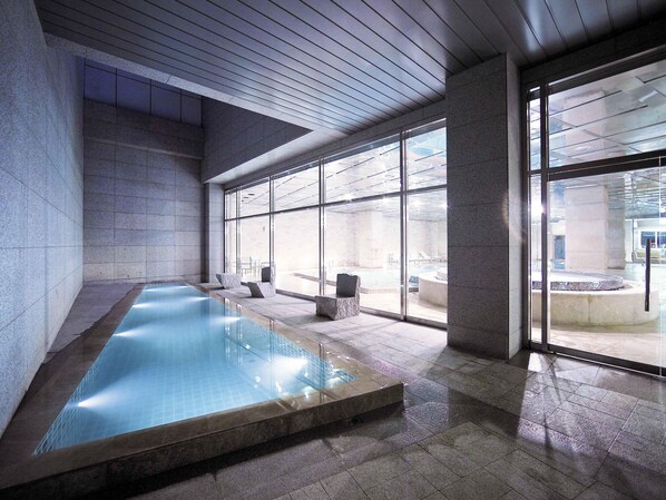 A modern indoor pool with clear glass walls, stone flooring, and a minimalist design. - Grand Mercure Ambassador Changwon (Changwon)