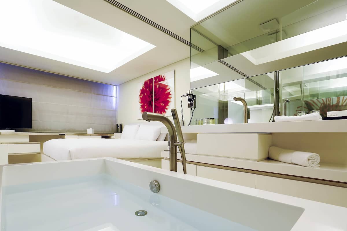 A modern bathroom with a large bathtub, a vanity with a mirror, and a television on the left.