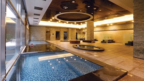 A modern indoor pool area with a glass enclosure, a central water feature, and a reception desk. - Grand Mercure Ambassador Changwon (Changwon)
