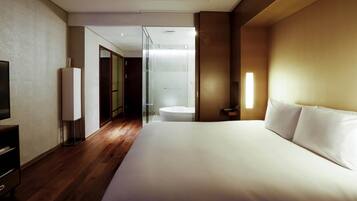 A modern hotel room with a large bed, a TV, a wardrobe, and a bathroom with a glass shower.