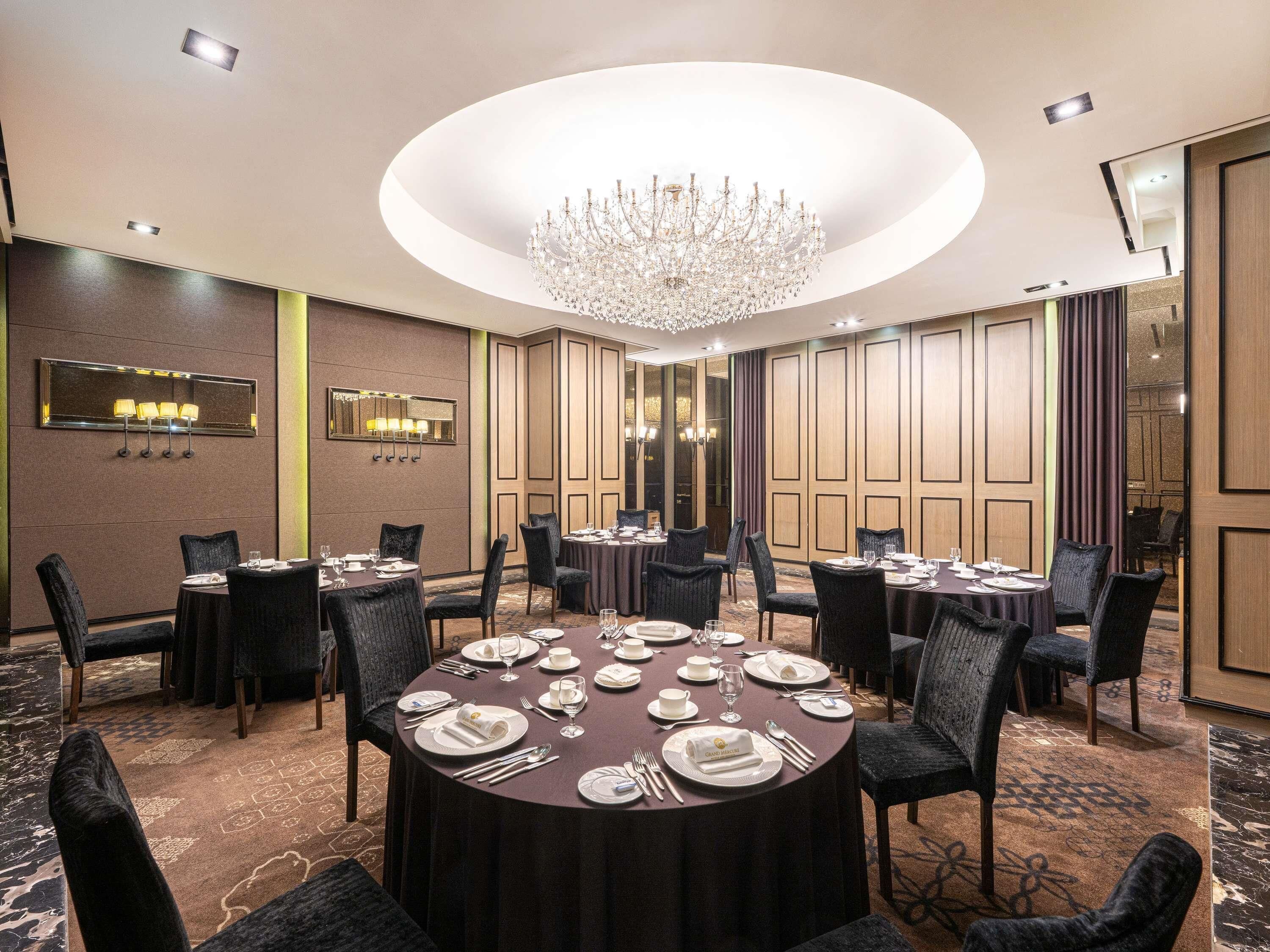 Un salón de conferencias con una mesa redonda dispuesta para una reunión, rodeado de sillas, y una araña colgante.