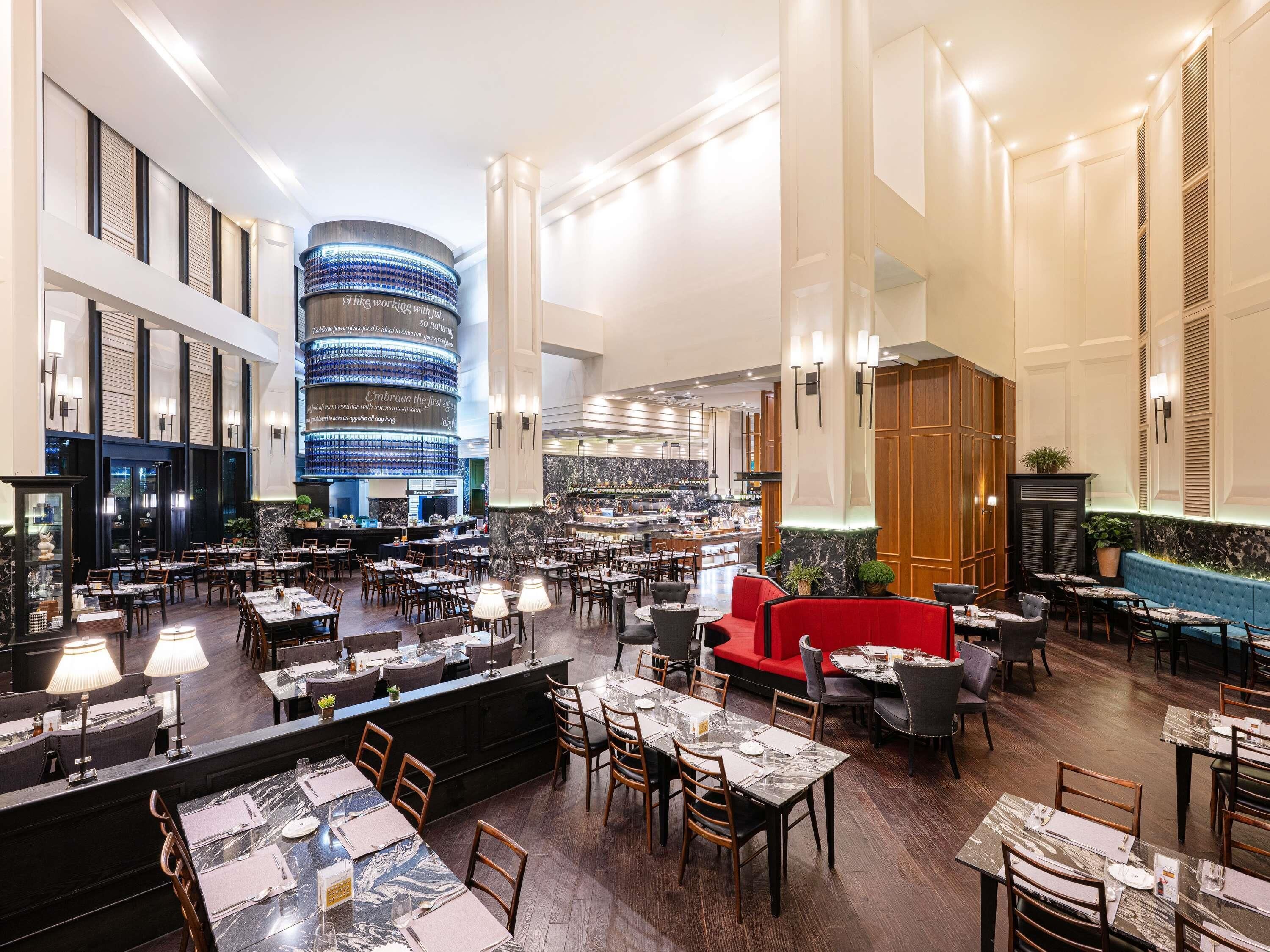 A spacious hotel lobby with multiple dining areas, a central bar, and a distinctive circular blue-lit structure.