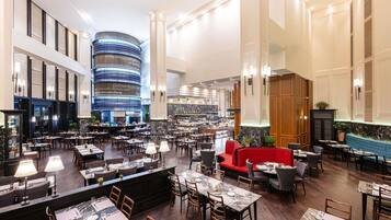 A spacious hotel lobby with multiple dining areas, a central bar, and a distinctive circular blue-lit structure.