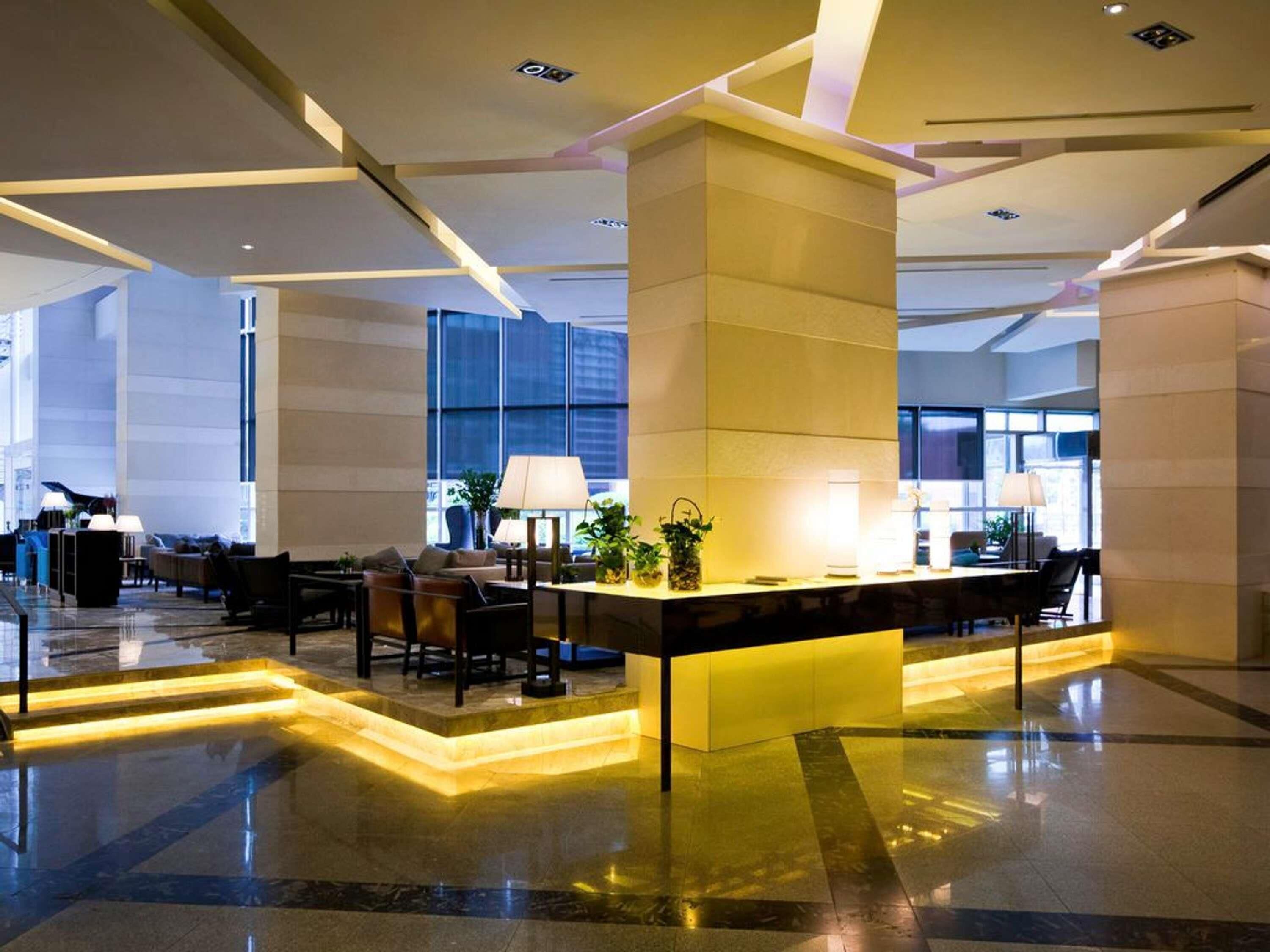 A modern hotel lobby with a reception desk, seating area, and large windows.