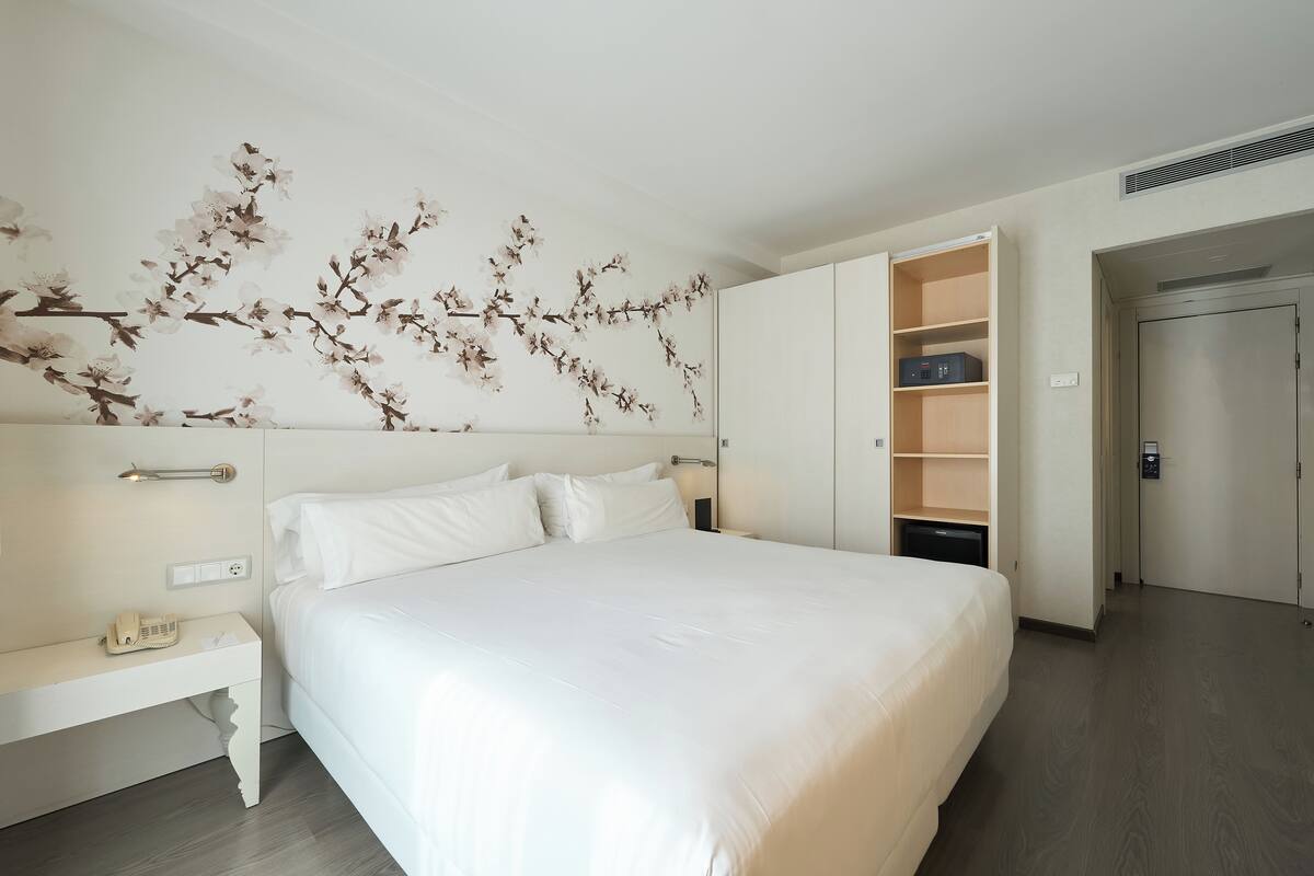 A modern hotel room with a large bed, a nightstand, a wardrobe, and a wall-mounted air conditioning unit.