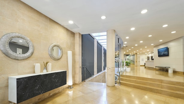 Un vestíbulo moderno con un mostrador de recepción de mármol, dos espejos en la pared y una escalera que conduce a los pisos superiores.