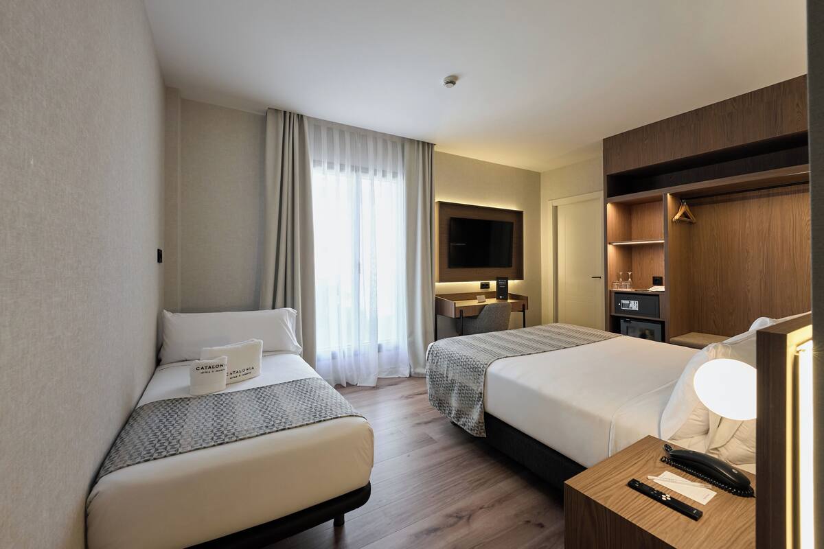 A hotel room with two beds, a desk, a TV, and a wardrobe.