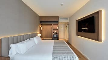 Habitación de hotel con una cama grande, un televisor montado en la pared, un armario y una mesita de noche.