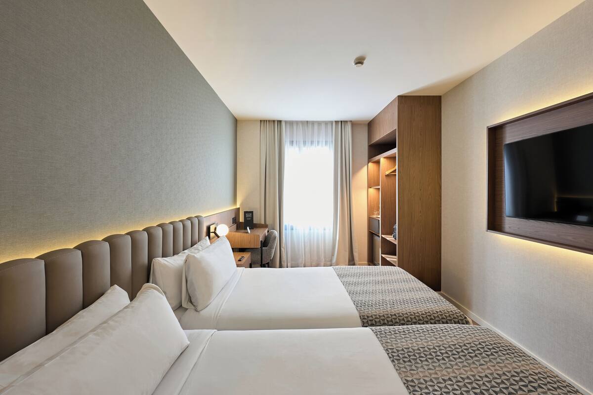 A hotel room with two beds, a desk, a TV, and a wardrobe.