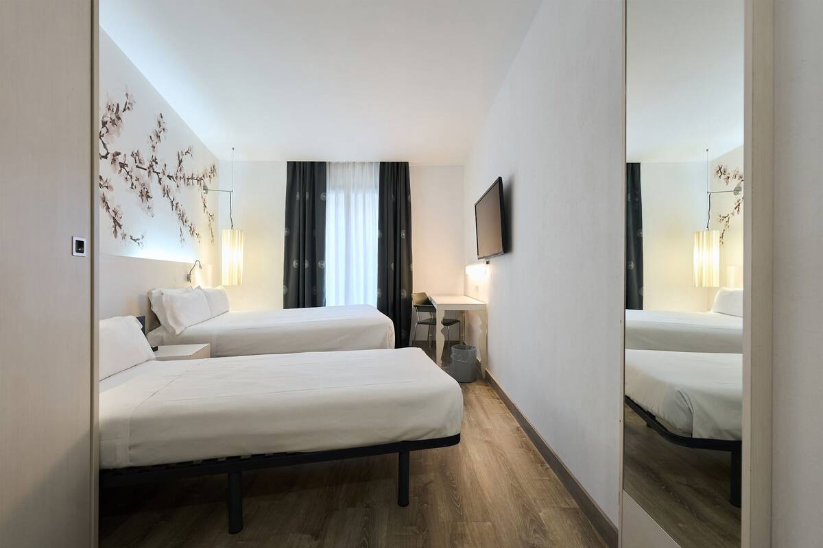 A hotel room with two beds, a desk, a chair, a TV, and a mirror.
