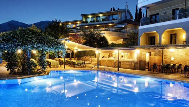 Une piscine entourée d’espaces de détente extérieurs et un bâtiment doté de nombreux balcons.