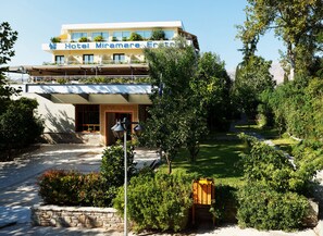 Um hotel com fachada moderna, entrada visível e área de jardim bem cuidada.