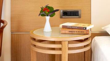 A wooden chair, a small round table with a white vase and a book, and a bed with a white pillow.