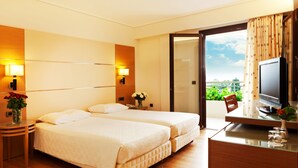 Une chambre d’hôtel avec deux lits, un bureau avec une télévision et une vue sur la verdure environnante.