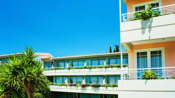 A multi-story hotel with balconies, a clear blue sky, and lush greenery.