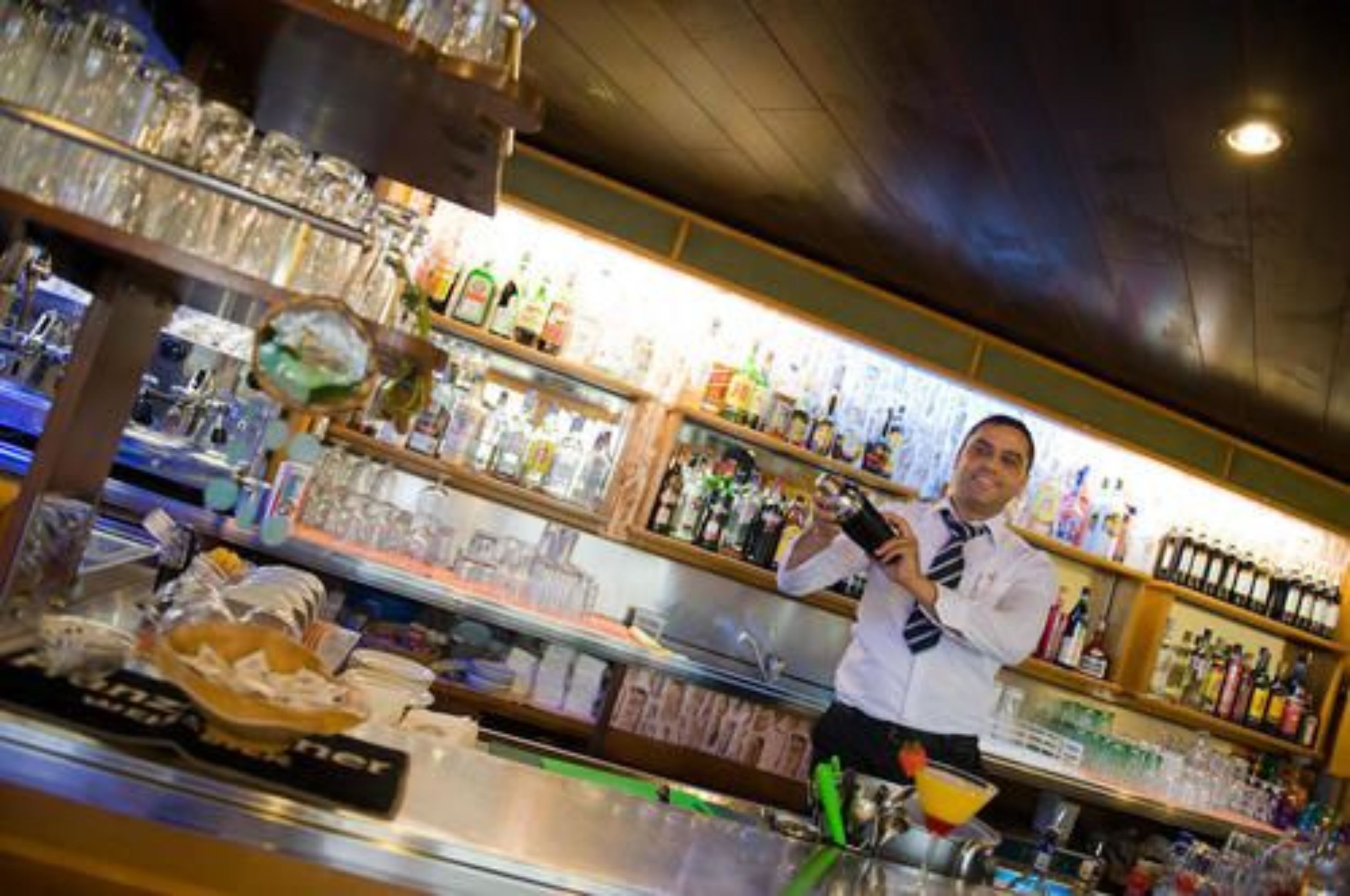 Zona de bar con estantes llenos de botellas y vasos.