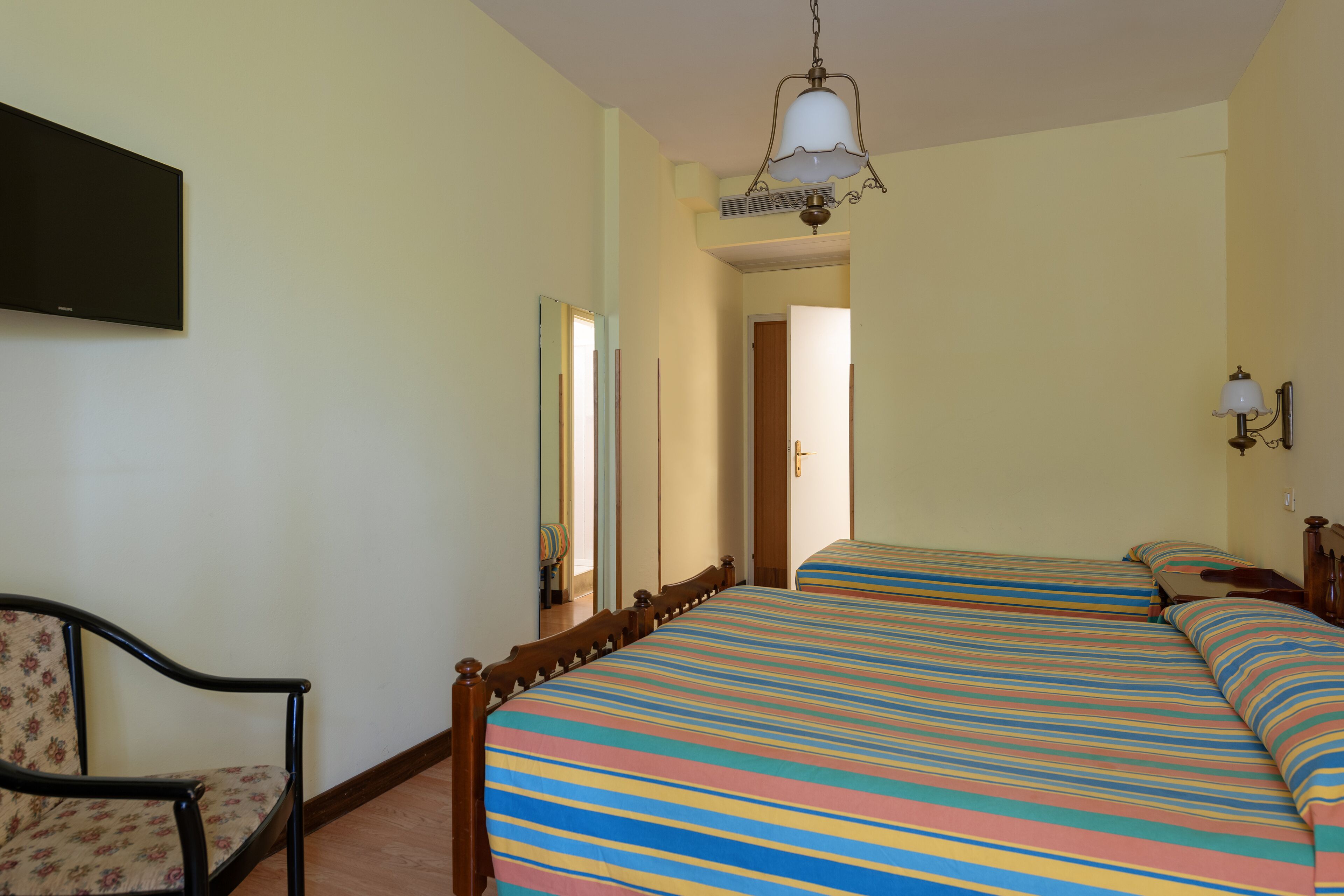 Een slaapkamer met een bed, een stoel, een spiegel en een plafondlamp.