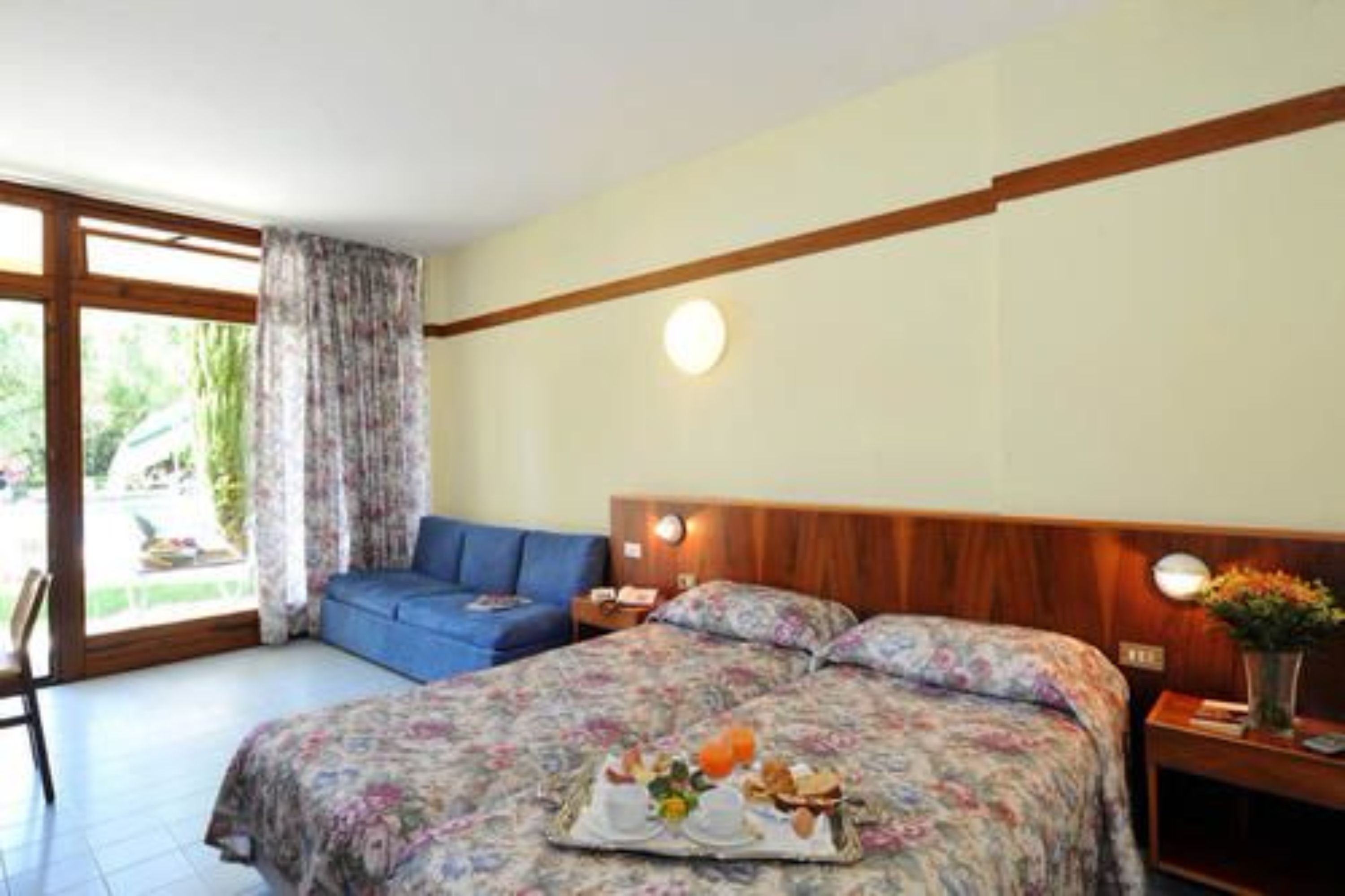 A bedroom with a bed, a nightstand, a blue chair, and a window with curtains.