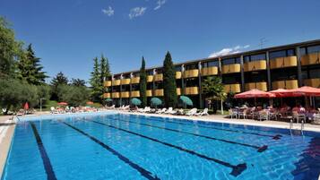 Piscina con sillas de descanso y sombrillas, rodeada por un edificio con varios balcones.