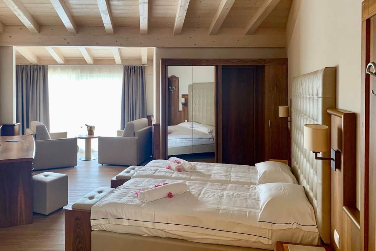 Ein Hotelzimmer mit Holzbalkendecke, einem Bett mit weißen Leinentextilien, einer Sitzecke mit Stühlen und einem großen Spiegel.