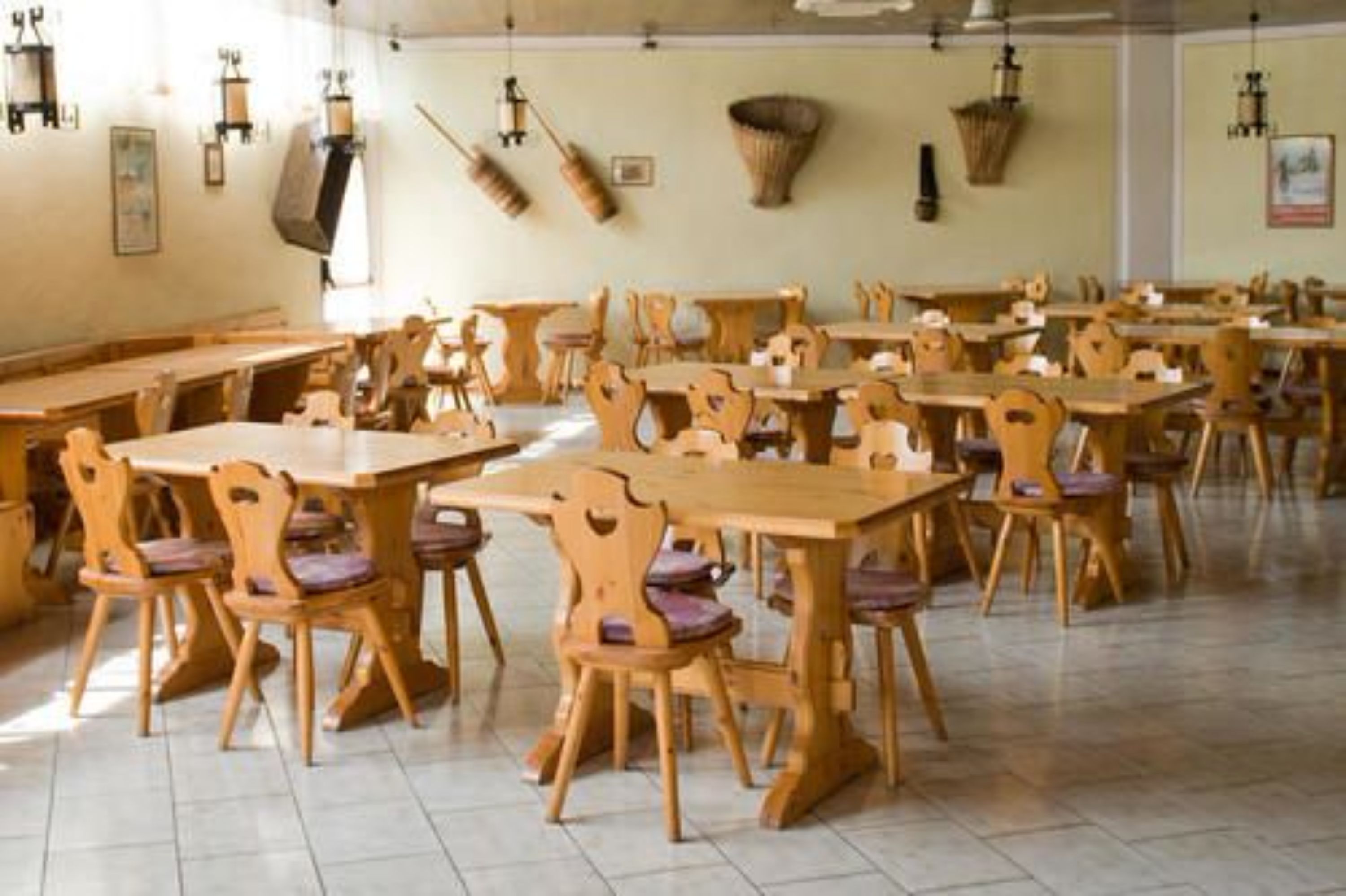 Un comedor con mesas y sillas de madera, suelo de baldosas y cestas colgadas en la pared.