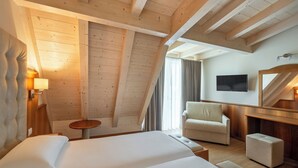 Hotellihuone, jossa on suuri sänky, oleskelualue, jossa on tuoli ja pieni pöytä, televisio ja peili.