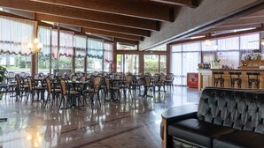 A spacious indoor area with tables and chairs, large windows, and a bar area. - Hotel Royal (Garda)