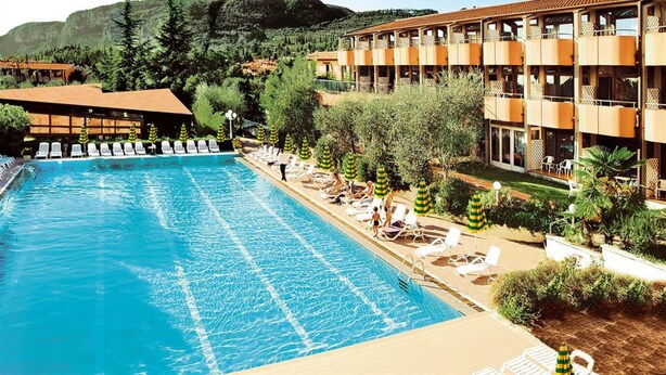 A hotel with a swimming pool, lounge chairs, and a mountain backdrop. - Hotel Royal (Garda)