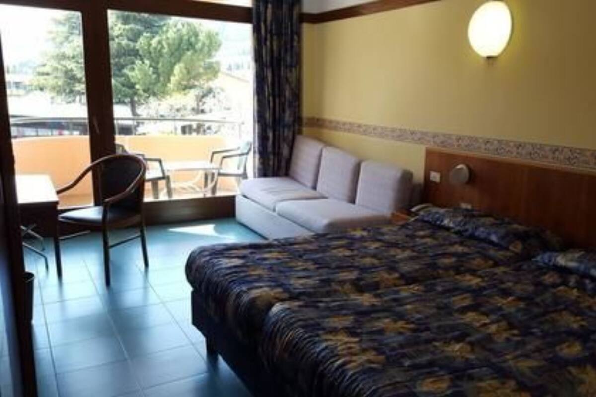 A hotel room with a bed, a sofa, a chair, and a balcony with a view of trees.