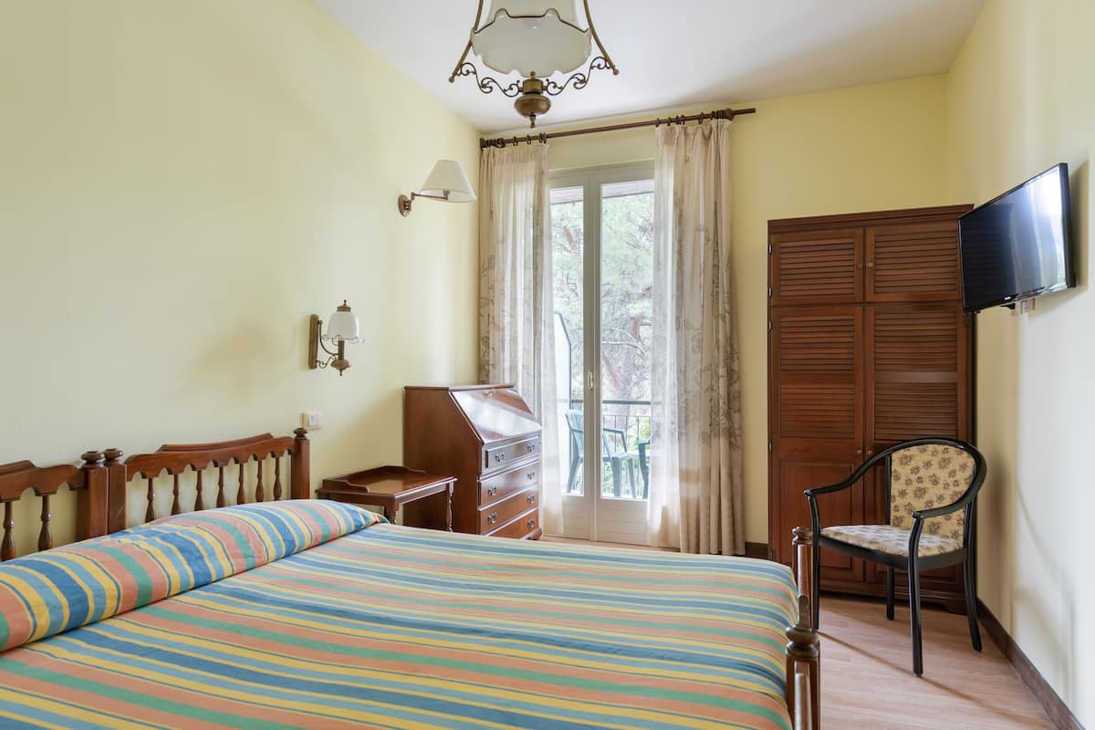 A bedroom with a bed, a dresser, a chair, a television, and a window with curtains.