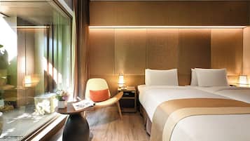Una habitación de hotel con una cama grande, mesitas de noche, una silla y una pequeña mesa con una lámpara.